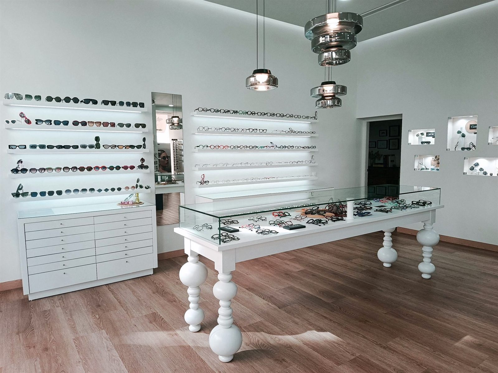 Sala principal de Senti2 con estanterías de gafas de sol, mesa vitrina de monturas y lámparas de cristal