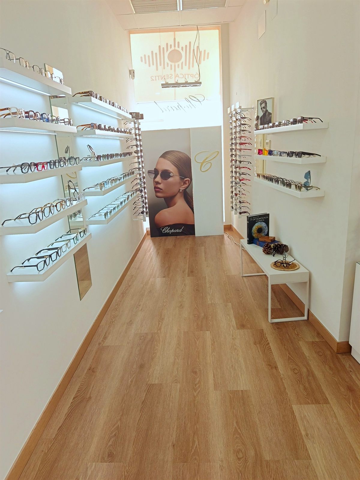 Pasillo de la óptica Senti2 con estanterías iluminadas de gafas graduadas y un cartel de Chopard al fondo